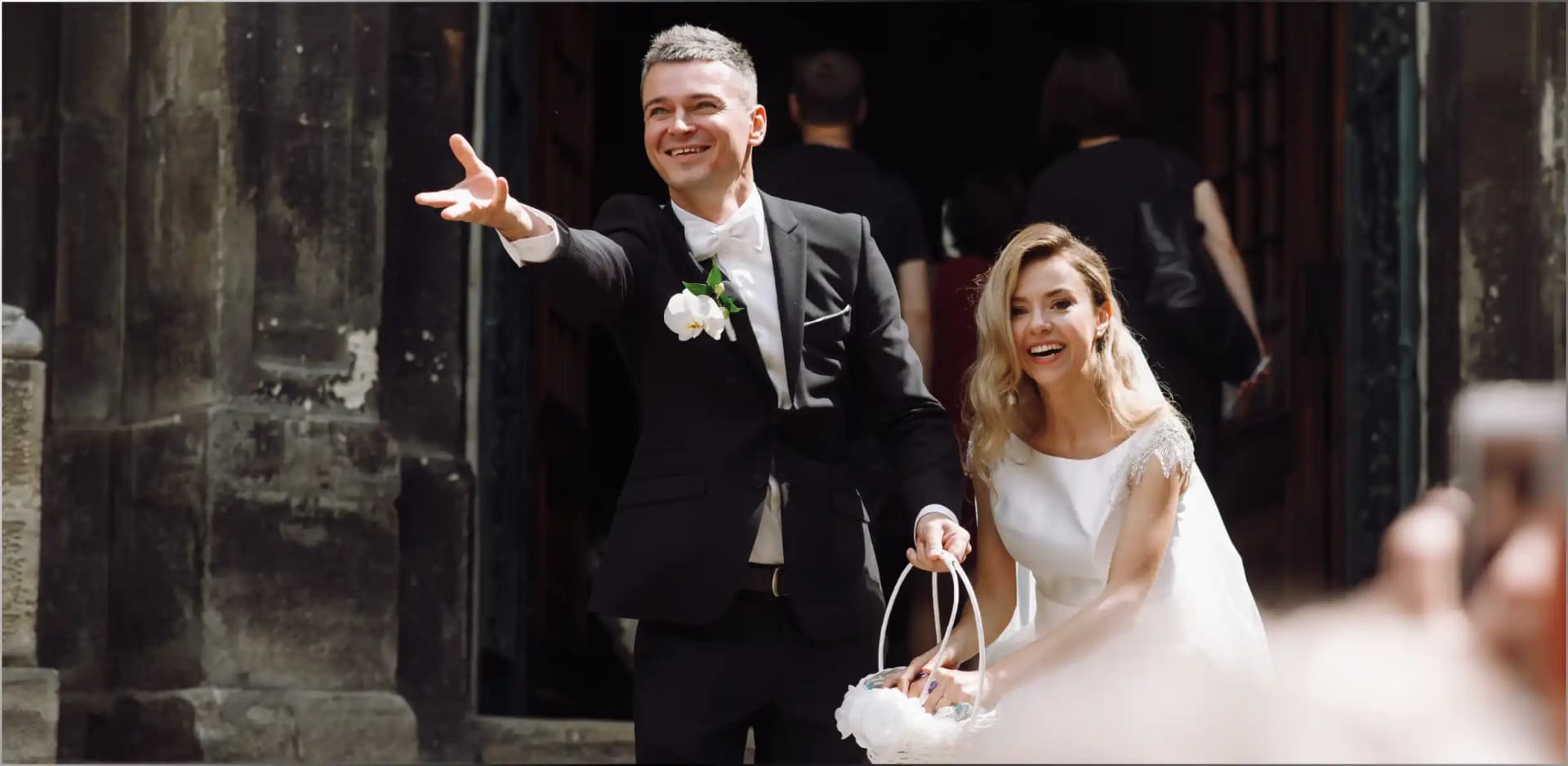 Bride and groom leaving a venue, the groom waving toward the camera